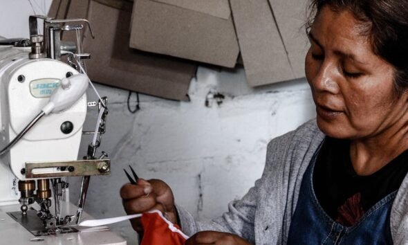Lima Metropolitana — Una mujer de rasgos asiáticos opera una máquina de coser industrial mientras sostiene una pieza de tela roja. Foto de: Gestión