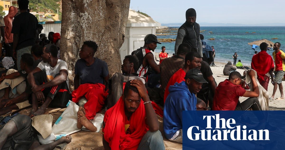 crisis migratoria Ceuta — Personas descansan bajo la sombra de un árbol en una playa de Ceuta tras el cruce masivo de la frontera. Foto de: The Guardian
