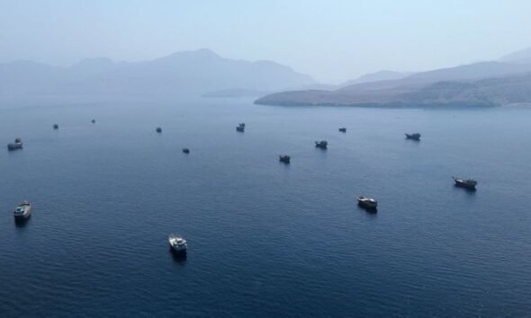 ataques EE.UU. Irán — Varios botes pequeños anclados en aguas tranquilas frente a una costa montañosa bajo un cielo brumoso. Foto de: CNN en Español