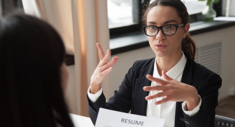Empresas restringen aumentos — Una mujer con gafas y traje oscuro gesticula mientras habla con otra persona frente a un documento que dice 'RESUME'. Foto de: Gestión