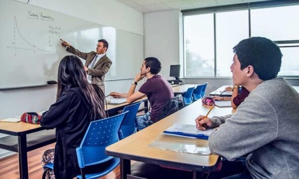 requisitos establecidos — Un profesor señala una gráfica en una pizarra mientras tres estudiantes escuchan en un salón de clases. Foto de: El Peruano