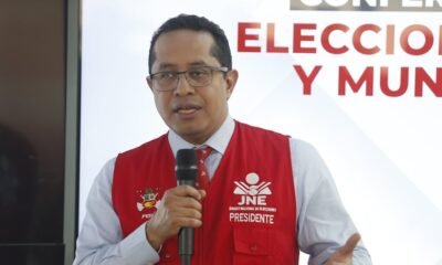 reelección inmediata — Un hombre con gafas y un chaleco rojo que dice JNE Presidente habla frente a un micrófono en un evento. Foto de: Gestión