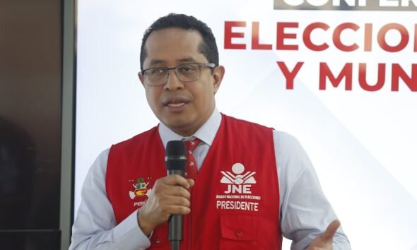 reelección inmediata — Un hombre con gafas y un chaleco rojo que dice JNE Presidente habla frente a un micrófono en un evento. Foto de: Gestión