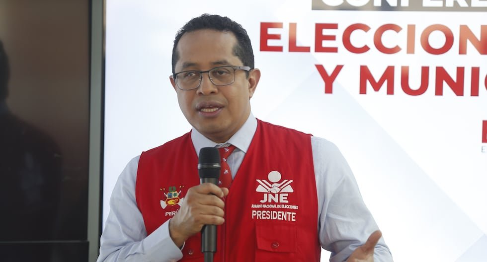 reelección inmediata — Un hombre con gafas y un chaleco rojo que dice JNE Presidente habla frente a un micrófono en un evento. Foto de: Gestión