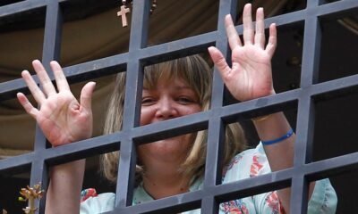Una mujer sonríe tras una reja metálica en un contexto que evoca la liberación de la jueza María Lourdes Afiuni. Foto de: Infobae