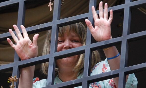 Una mujer sonríe tras una reja metálica en un contexto que evoca la liberación de la jueza María Lourdes Afiuni. Foto de: Infobae