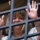 Una mujer sonríe tras una reja metálica en un contexto que evoca la liberación de la jueza María Lourdes Afiuni. Foto de: Infobae