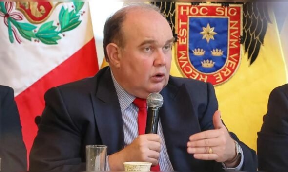 López Aliaga — Un hombre con traje oscuro y corbata roja habla por un micrófono frente a banderas con escudos heráldicos. Foto de: La República