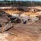 ley MAPE — Vista aérea de una mina de arena con maquinaria pesada, camiones y estructuras de procesamiento en un terreno de tierra y agua. Foto de: Gestión